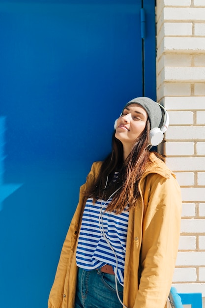 mujer apoyada en la pared usando auriculares con los ojos cerrados