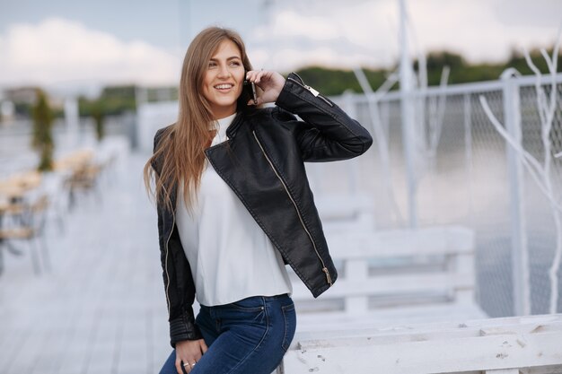 Mujer apoyada en una tabla de madera blanca hablando por teléfono mientras sonrie