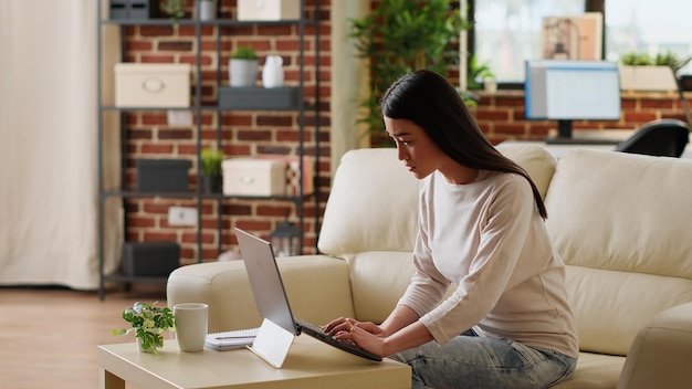 Mujer apresurada que trabaja de forma remota en una computadora portátil mientras desarrolla un proyecto de inicio debido a la fecha límite temprana. Hermosa freelancer haciendo trabajo remoto en una computadora moderna mientras desarrolla ideas de negocios en casa.