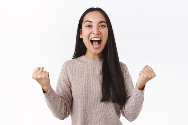 La mujer aprieta los puños con un poderoso movimiento triunfal, bombea el puño y grita que sí de asombro y alegría, sonriendo complacida, logra el éxito, recibe el premio.