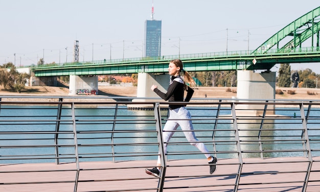 Mujer apta de los jóvenes en ropa deportiva que corre cerca del río idílico