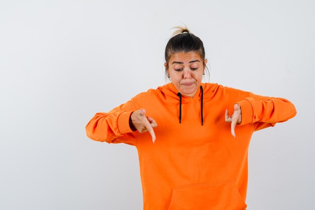 Mujer apuntando hacia abajo en sudadera con capucha naranja y mirando enfocado