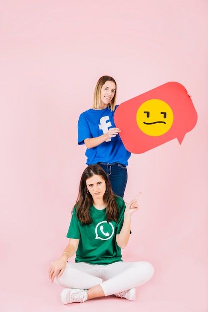 Mujer apuntando hacia arriba en frente de su amigo sosteniendo el bocadillo de diálogo emoji triste