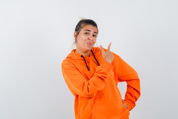 Mujer apuntando hacia arriba con una sudadera con capucha naranja y luciendo linda