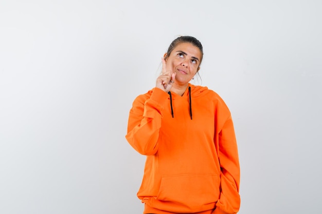 Mujer apuntando hacia arriba con una sudadera con capucha naranja y luciendo linda