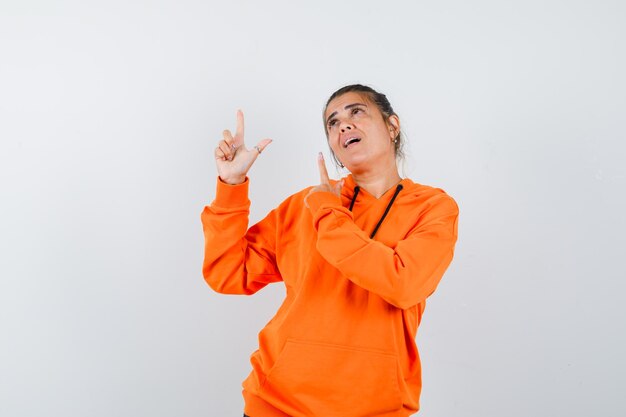 Mujer apuntando hacia arriba en sudadera con capucha naranja y mirando soñadora