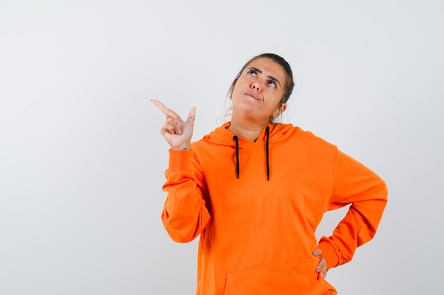 Mujer apuntando a la esquina superior izquierda en sudadera con capucha naranja y mirando pensativo