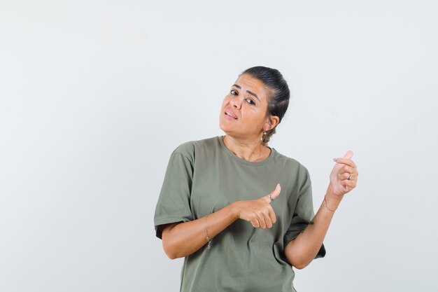 Mujer apuntando a un lado con los pulgares en la camiseta y mirando vacilante