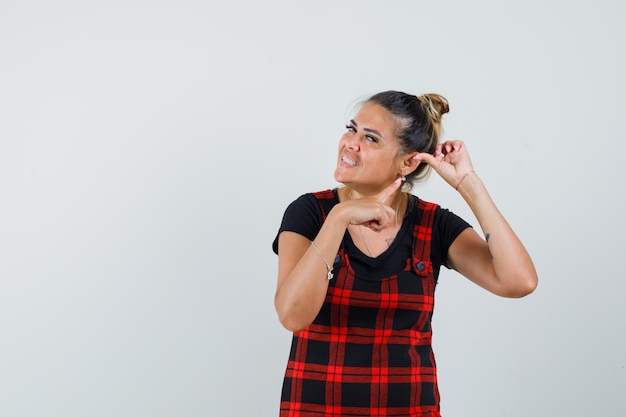 Mujer apuntando a su oreja con vestido delantal, vista frontal.