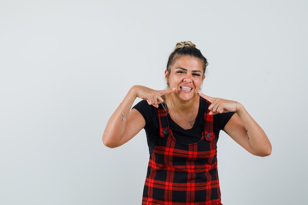 Mujer apuntando a sus dientes en vista frontal del vestido delantal.