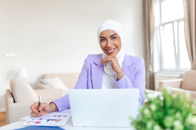 Mujer árabe atractiva que trabaja en una computadora portátil y papeleo en el escritorio Mujer de negocios árabe que trabaja en casa Dedicación y tecnología Esencial para realizar sus tareas