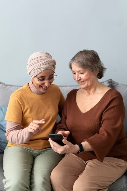 La mujer árabe le está enseñando a la mujer mayor a usar un teléfono inteligente en la sala de estar