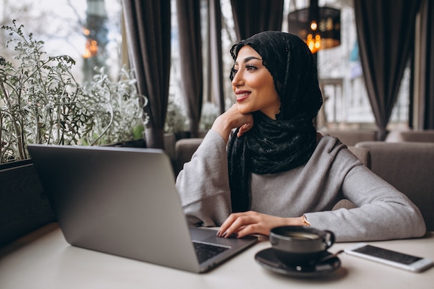 Mujer árabe en hijab dentro de un café trabajando en una computadora portátil