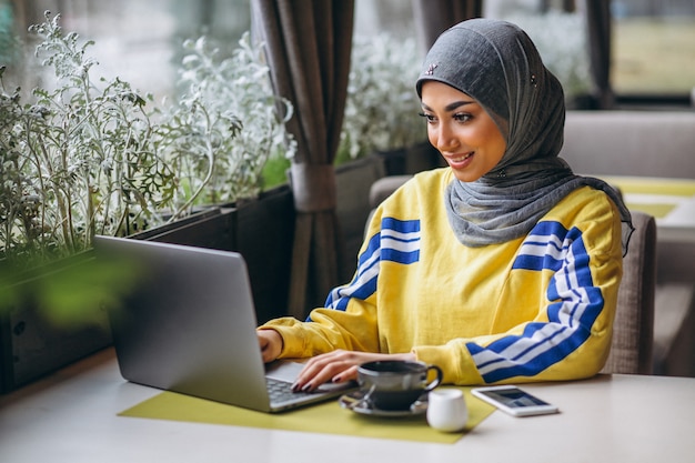 Mujer árabe en hijab dentro de un café trabajando en una computadora portátil