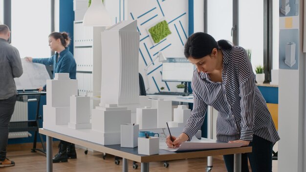 Mujer arquitecta analizando el plan de planos en la mesa para diseñar el modelo de construcción y la maqueta. Ingeniero que trabaja en un proyecto de desarrollo arquitectónico con herramientas de construcción industrial.