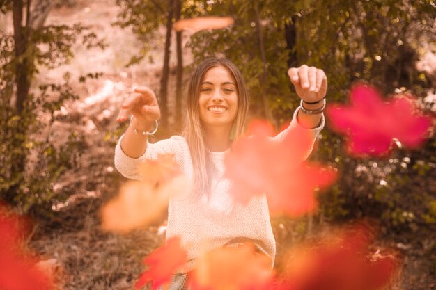 Mujer arrojando hojas de otoño a la cámara