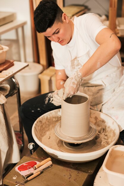 Mujer artesana formando una vasija de barro en un torno de alfarero.