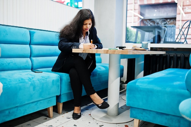 Mujer artista india usa pintura formal y escucha música hindú desde los auriculares mientras está sentada en el café