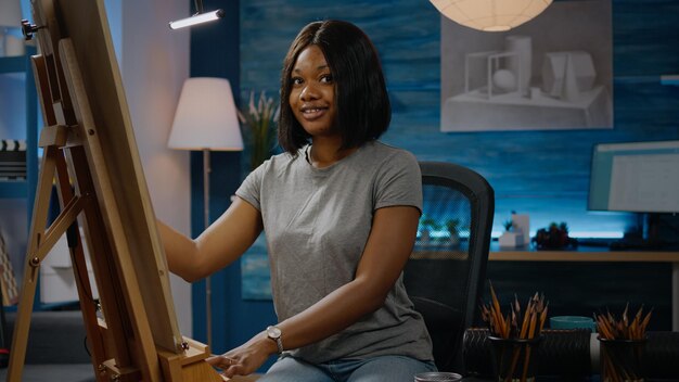 Mujer artística negra sentada en el estudio del taller y jarrón de dibujo con lápiz sobre lienzo blanco. Artista joven afroamericano que trabaja en una obra maestra moderna con herramientas e instrumentos de arte