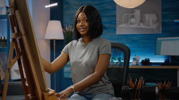 Mujer artística negra sentada en el estudio del taller y jarrón de dibujo con lápiz sobre lienzo blanco. Artista joven afroamericano que trabaja en una obra maestra moderna con herramientas e instrumentos de arte