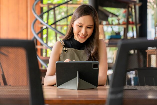 Mujer asiática adulta diseñadora creativa felicidad pensando en el trabajo y la investigación y tomando nota de ideas interesantes a través de una tableta