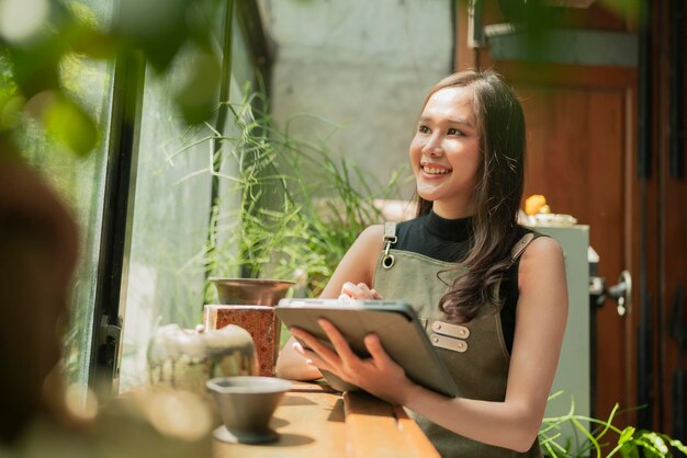 Mujer asiática adulta diseñadora creativa felicidad pensando en el trabajo y la investigación y tomando nota de ideas interesantes a través de una tableta