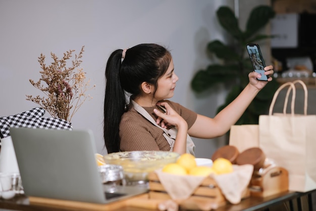 Mujer asiática adulta joven que prepara la panadería casera y el selfie en la cocina en casa