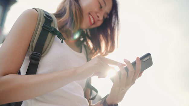 Mujer asiática alegre del blogger del backpacker que usa el smartphone para la dirección y que mira en mapa de ubicación