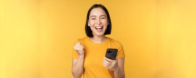 Mujer asiática alegre celebrando sostener el teléfono móvil ganando lograr el objetivo en el teléfono inteligente de pie