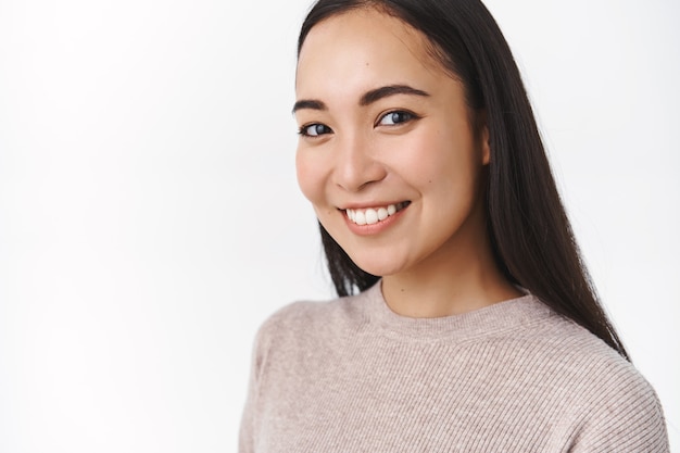 Mujer asiática alegre sonriente sana y activa, sonriendo feliz y mirando la cámara con la cabeza inclinada, riendo, comenzó una nueva rutina diaria de cuidado de la piel