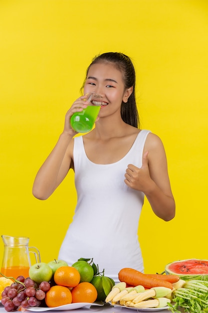 Mujer asiática Beber jugo de manzana, y sobre la mesa hay muchas frutas.