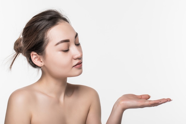 Mujer asiática de la belleza del cuidado de la piel del cuerpo que muestra el producto en lado con la presentación abierta de la mano y exhibición aislada en la pared blanca.