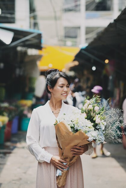 Mujer asiática bien vestida caminando por el mercado y llevando gran ramo de flores