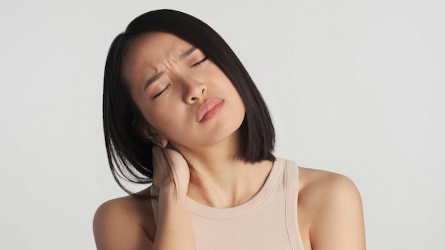 Mujer asiática cansada y molesta que siente dolor en el cuello y la cabeza después de un día duro de pie sobre fondo blanco Mujer con exceso de trabajo