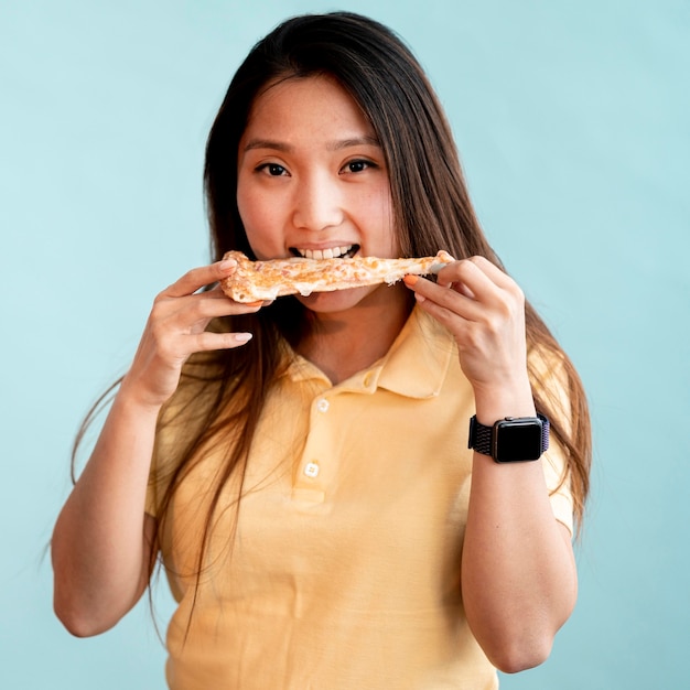 Mujer asiática comiendo una rebanada de pizza