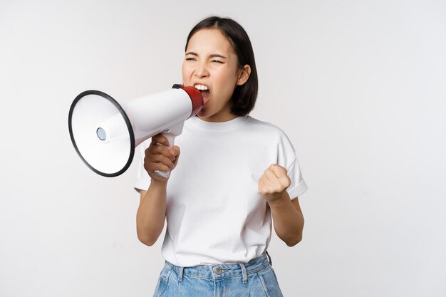 Mujer asiática confiada gritando en megáfono gritando y protestando Chica activista usando altavoz para hablar más fuerte de pie sobre fondo blanco