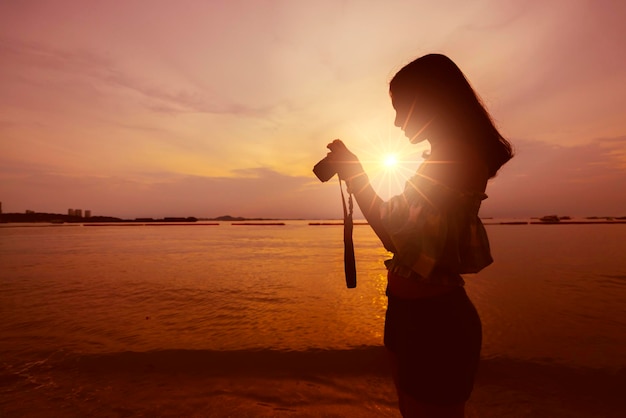 La mujer asiática disfruta tomando fotos con la cámara en el crepúsculo del atardecer en la playa