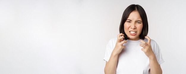 Mujer asiática enojada maldiciendo luciendo indignada y molesta apretando los dientes y frunciendo el ceño furioso de pie ov