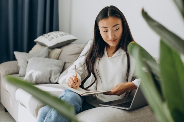 Mujer asiática estudiando en casa y leyendo en el sofá