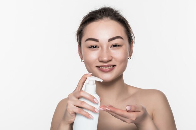 La mujer asiática exprime la loción de mano aislada en la pared blanca.