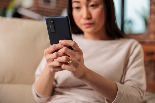 Mujer asiática feliz de aspecto auténtico casual que usa un teléfono inteligente en casa, tecnología de Internet web usuario de teléfono inteligente mensaje móvil dispositivo digital de comunicación de redes sociales