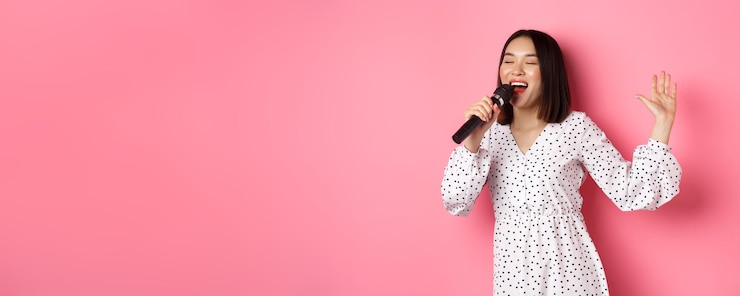 Foto gratuito mujer asiática feliz bailando y cantando en el micrófono actuando en el karaoke de pie sobre centrico rosa