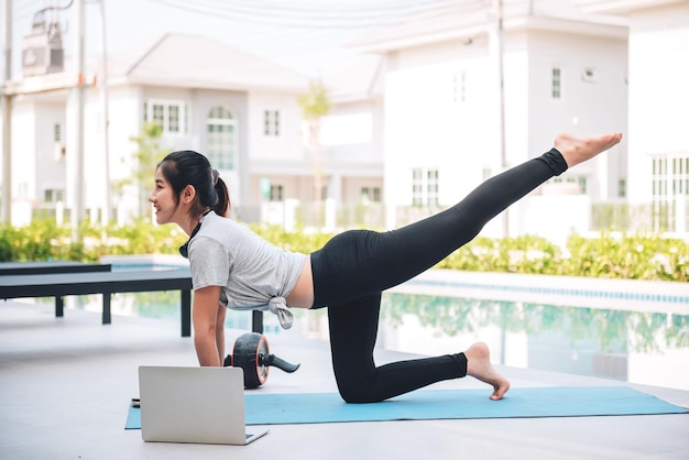 Mujer asiática feliz haciendo ejercicio de estiramiento y entrenamiento de yoga por la mañana en casa al aire libre