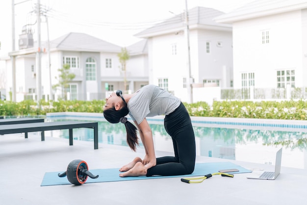 Mujer asiática feliz haciendo ejercicio de estiramiento y entrenamiento de yoga por la mañana en casa al aire libre