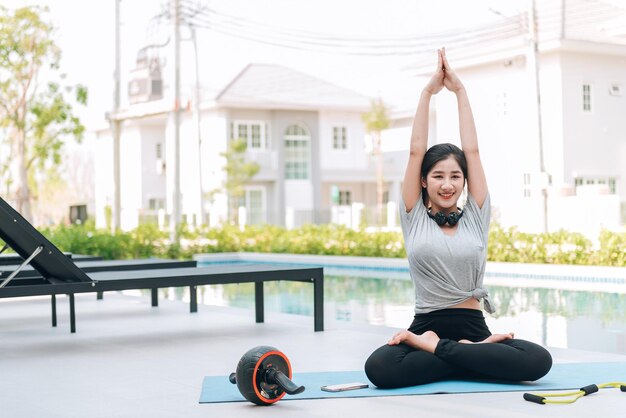 Mujer asiática feliz haciendo ejercicio de estiramiento y entrenamiento de yoga por la mañana en casa al aire libre