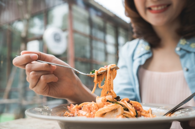 Mujer asiática feliz hermosa que come un plato de espagueti italiano de los mariscos en el restaurante o el café mientras que