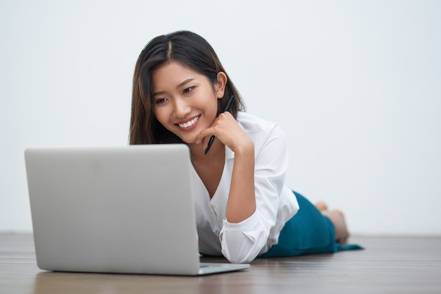 Mujer asiática feliz que trabaja en la computadora portátil en el piso