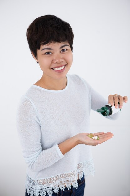 Mujer asiática feliz que vierte las píldoras de la botella