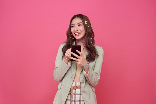 Mujer asiática feliz y sonriente de veinte años usando teléfono móvil aislada sobre un fondo rosado