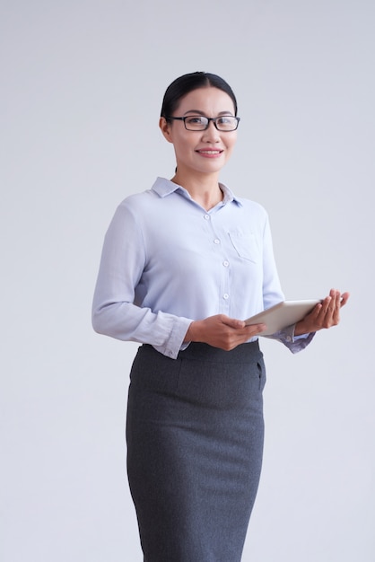 Mujer asiática en gafas, blusa elegante y falda posando en estudio con tableta